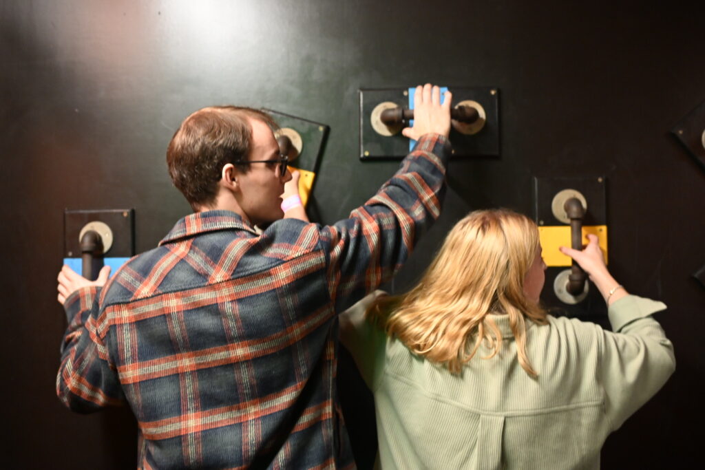 Two people climbing on a wall using handles made of metal pipe.