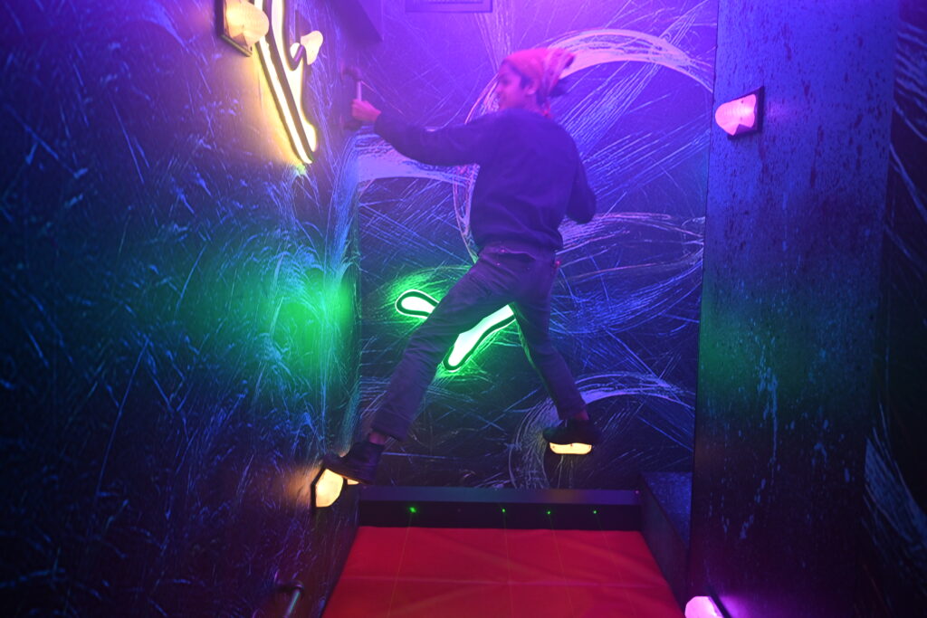 A woman climbs on glowing rock grips in a dark room.