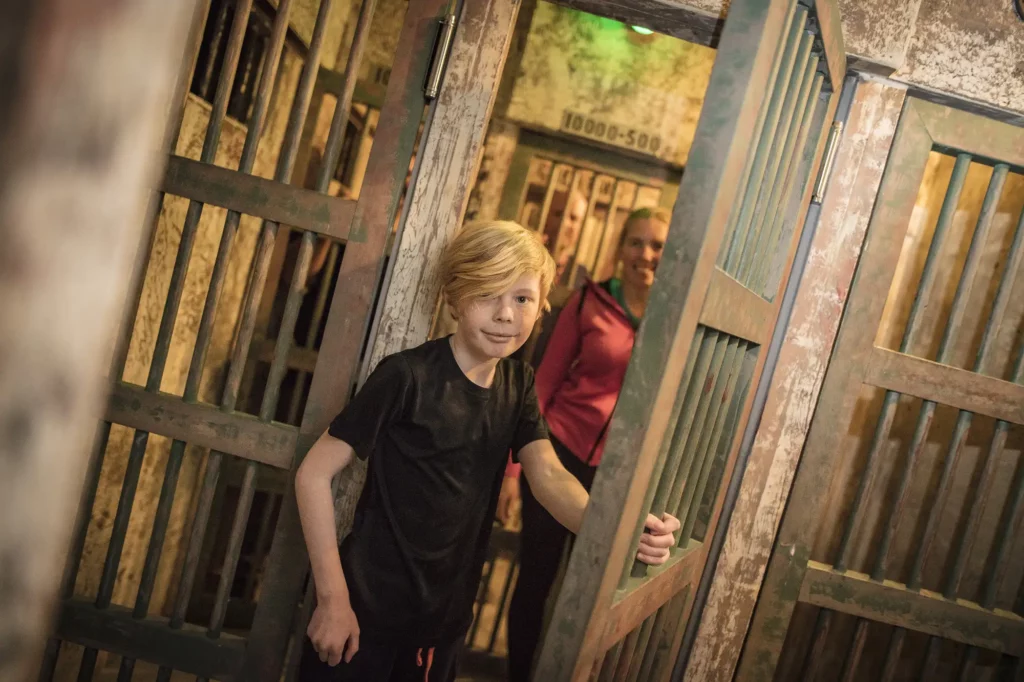 En kille står i dörröppningen till en fängelsecell med familjen i celler bakom sig