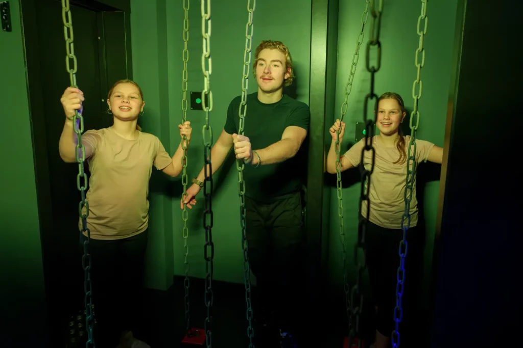 två tjejer och en kille håller i kedjor, som går från golv till tak