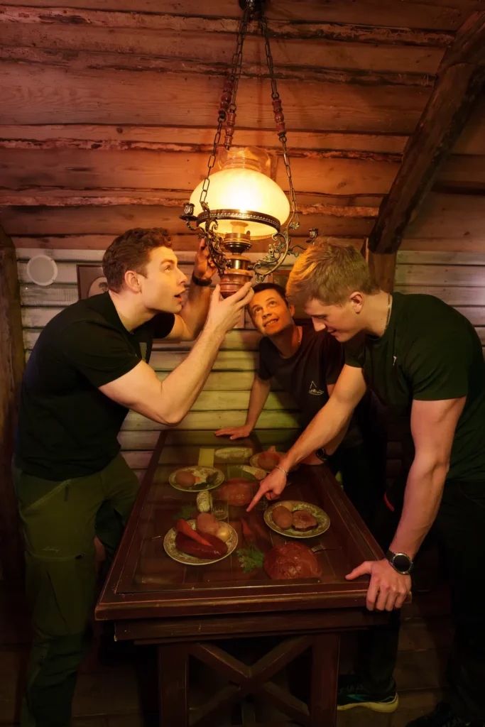 tre killar står vid ett matbord, en pekar på bordet, två fokuserar på lampan över bordet