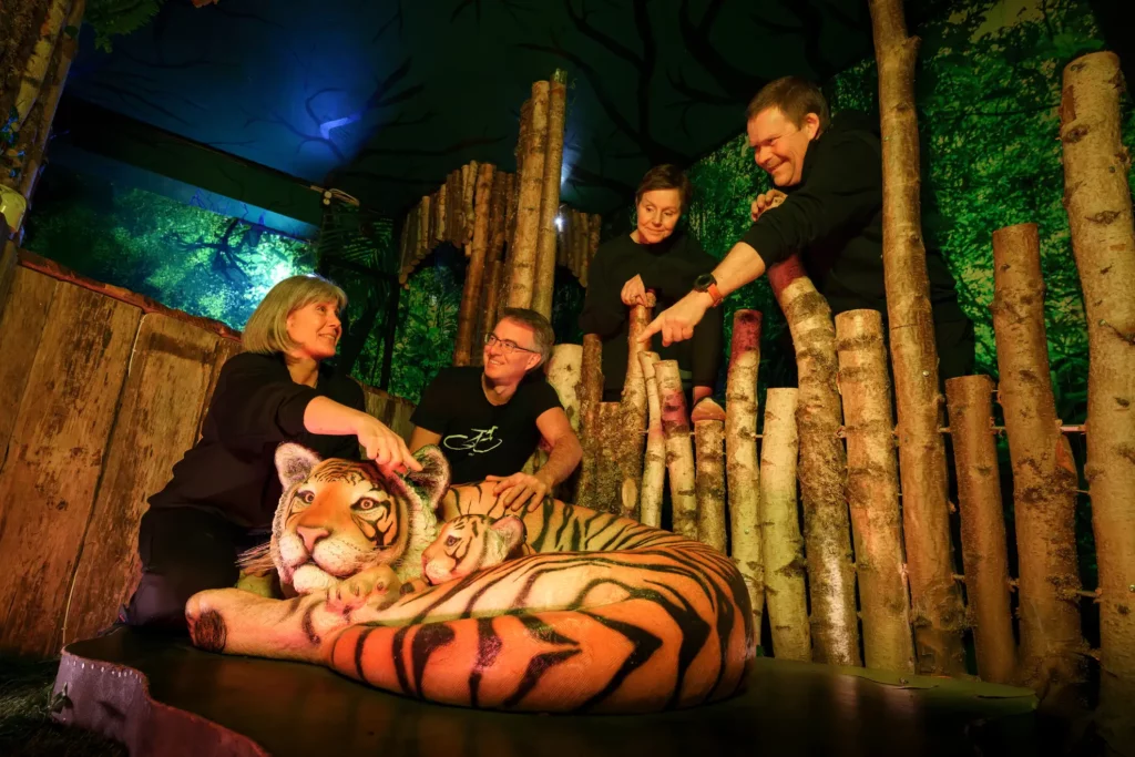 Fyra personer i ett rum varav två personer, pekar på tigern i mitten av rummet