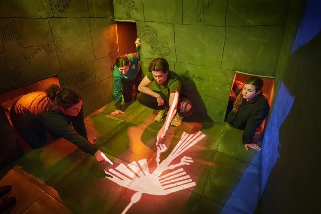 fyra personer sitter ned och pekar på en stor symbol, av en fågel, som lyser på golvet